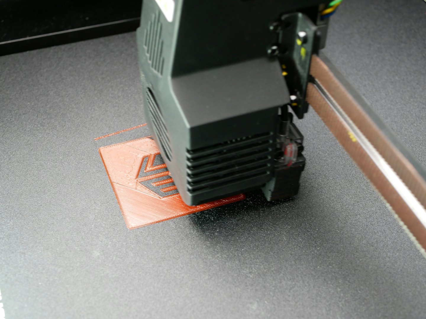 Drukarka 3D wytłaczająca pomarańczowy filament tworzący mały przedmiot.