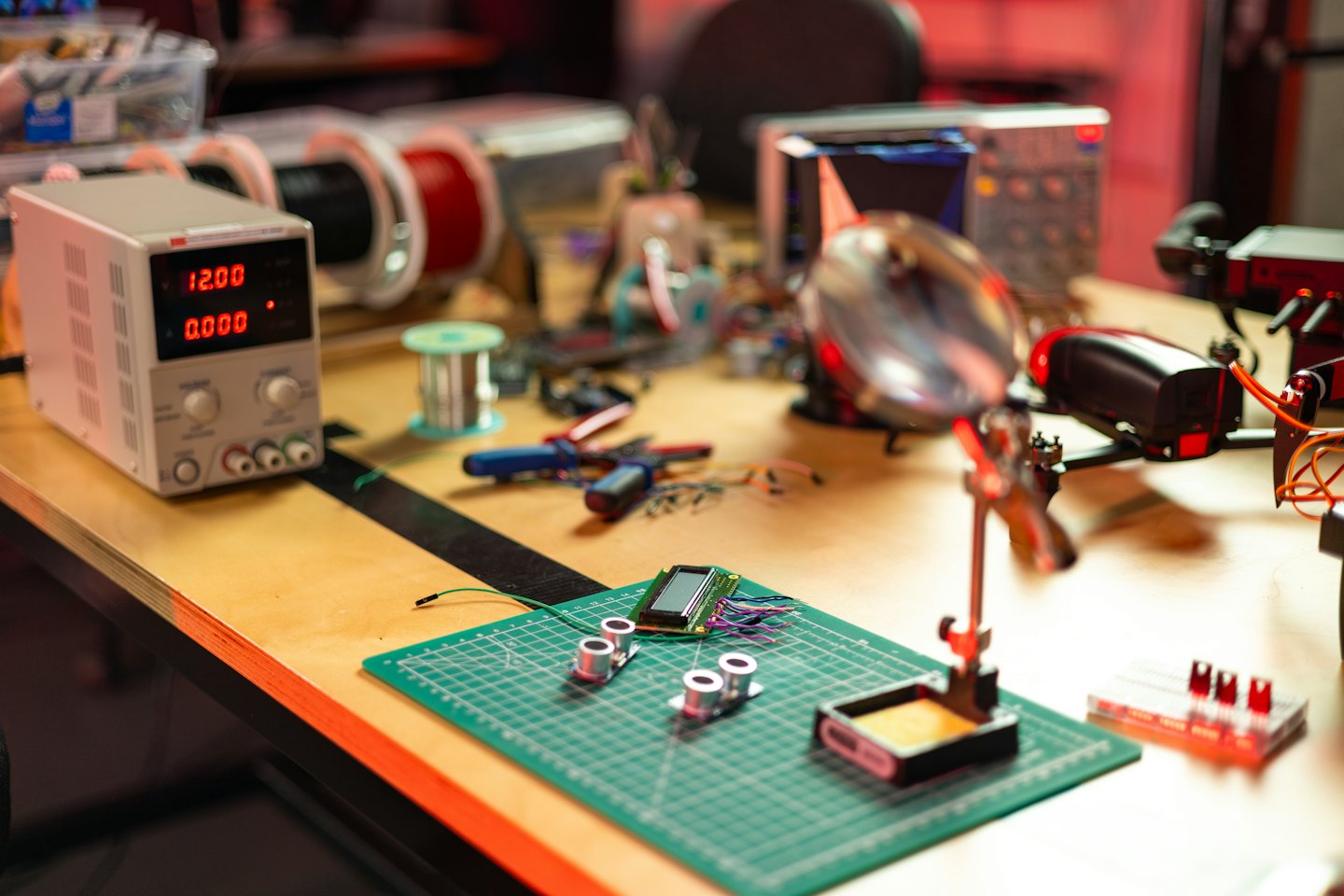 Elektroniczne komponenty i narzędzia ułożone na zielonej macie warsztatowej.